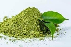 close up photo of heap of matcha powder with green tea leaves on white background
