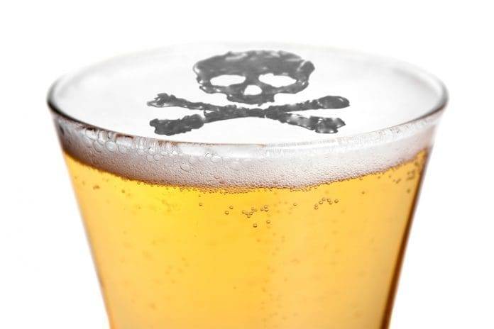The dangers of alcoholism concept with a skull and cross bones symbol floating on top of the beer.