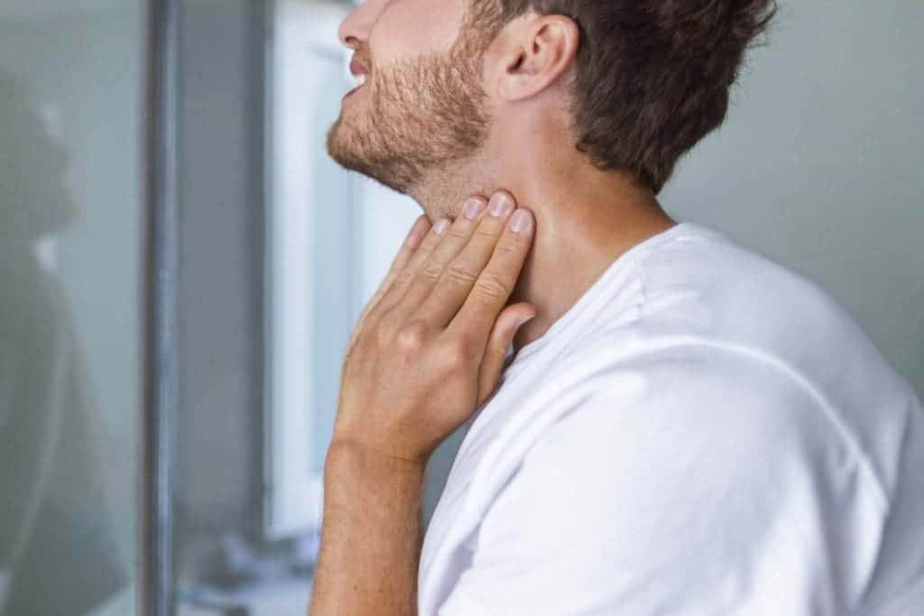 32929598 thyroid self exam checkup young man touching his neck at home bathroom doing self check of his thyroid gland looking at mirror for early signs of health problem