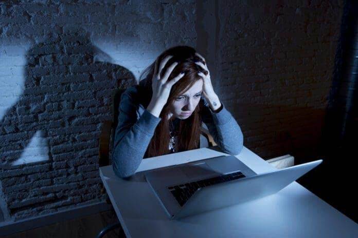 sad and scared female teenager with computer laptop suffering cyberbullying and harassment being online abused by stalker or gossip feeling desperate and humiliated in cyber bullying concept.