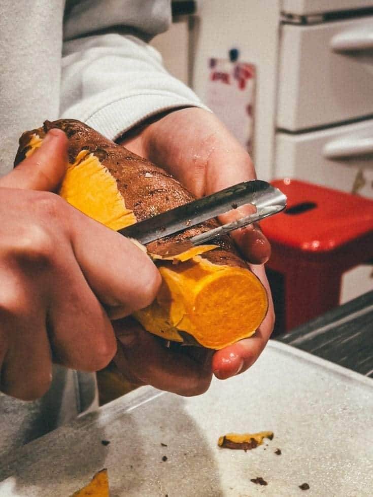 A person peeling a sweet potato.