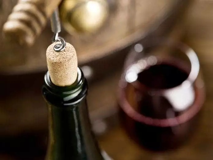 Opening of a wine bottle with corkscrew with wooden barrel on the background.